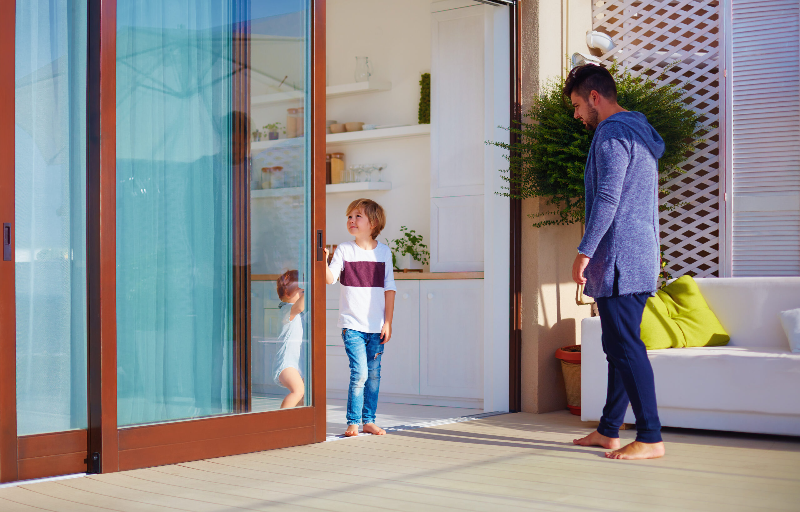 young boy opening a sliding patio door to step outside onto a nice patio with his father